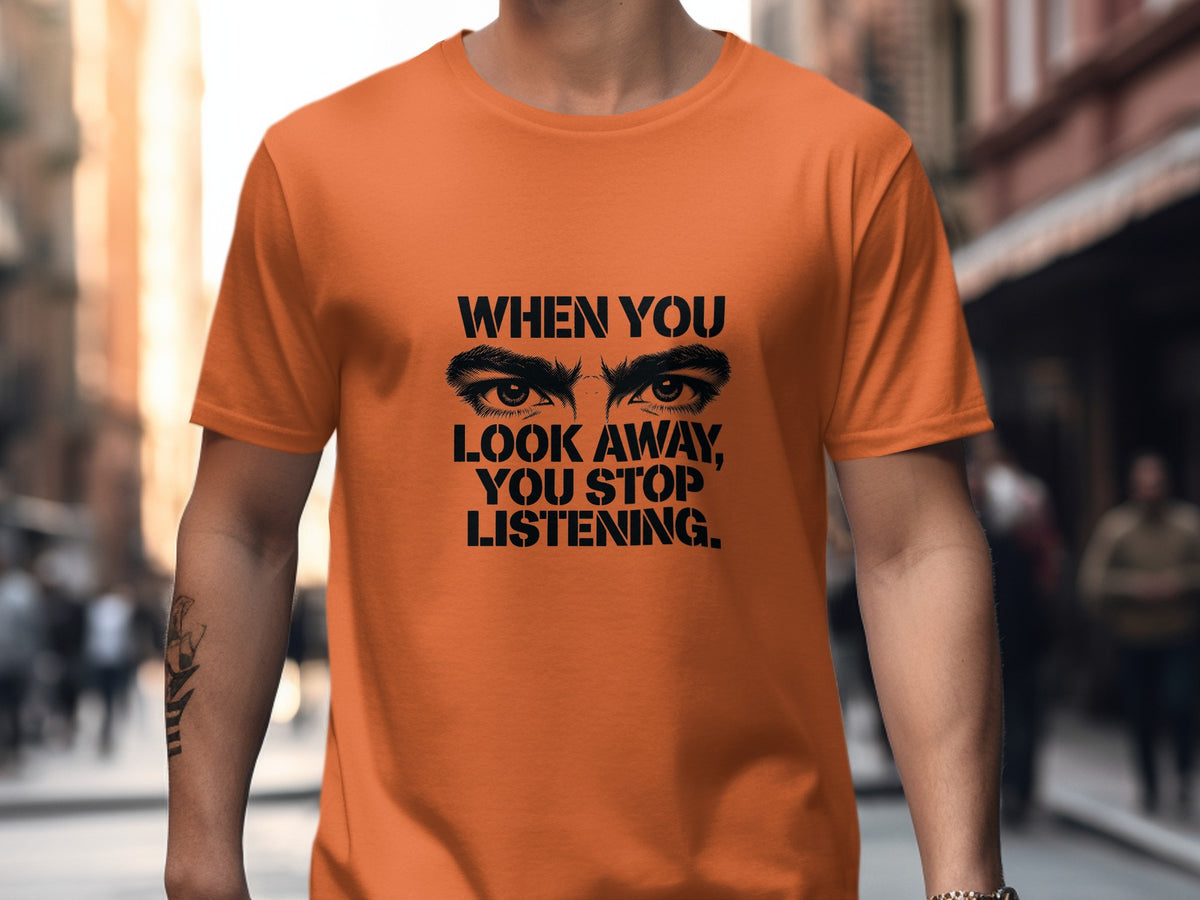 Orange t-shirt with black text that reads "WHEN YOU LOOK AWAY, YOU STOP LISTENING."