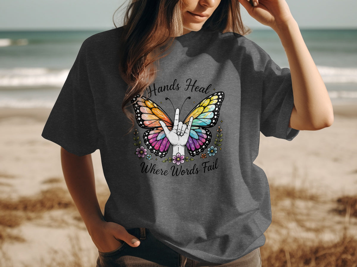 Butterfly graphic with "Hands Heal Where Words Fail" text and hand gesture on charcoal t-shirt.