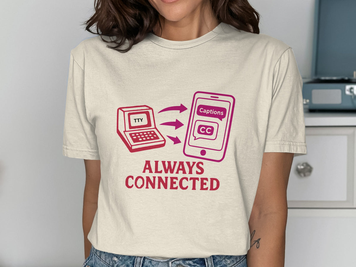Cream t-shirt with graphic of laptop labeled "TTY" connected to phone showing "Captions CC."