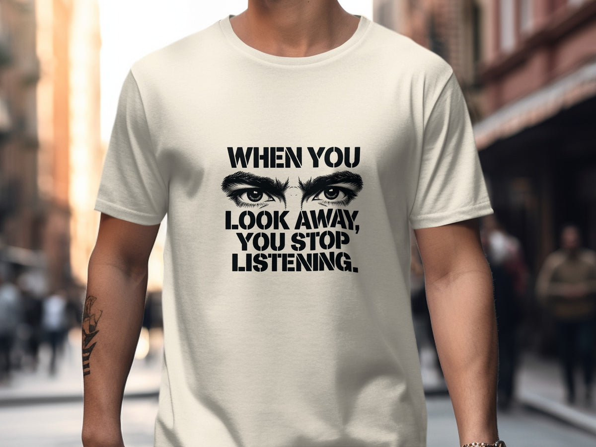 Cream t-shirt with black graphic of eyes and text "WHEN YOU LOOK AWAY, YOU STOP LISTENING."