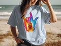 Light blue t-shirt with colorful chicken and hand graphic on a beach.