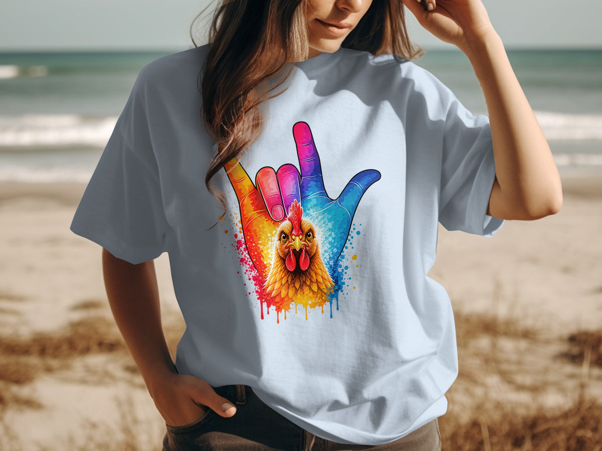 Light blue t-shirt with colorful chicken and hand graphic on a beach.