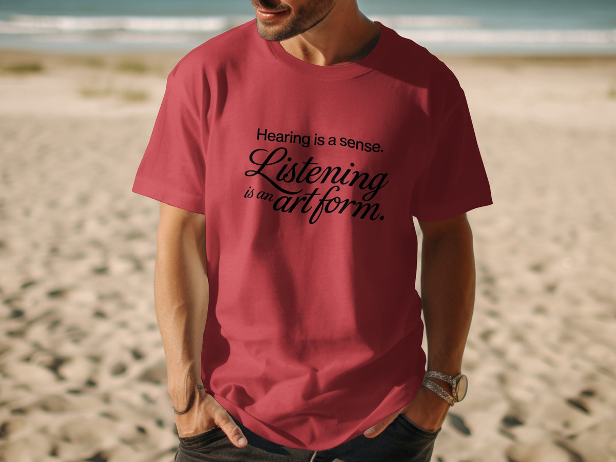 Red t-shirt with "Listening is an art form." text on a beach.
