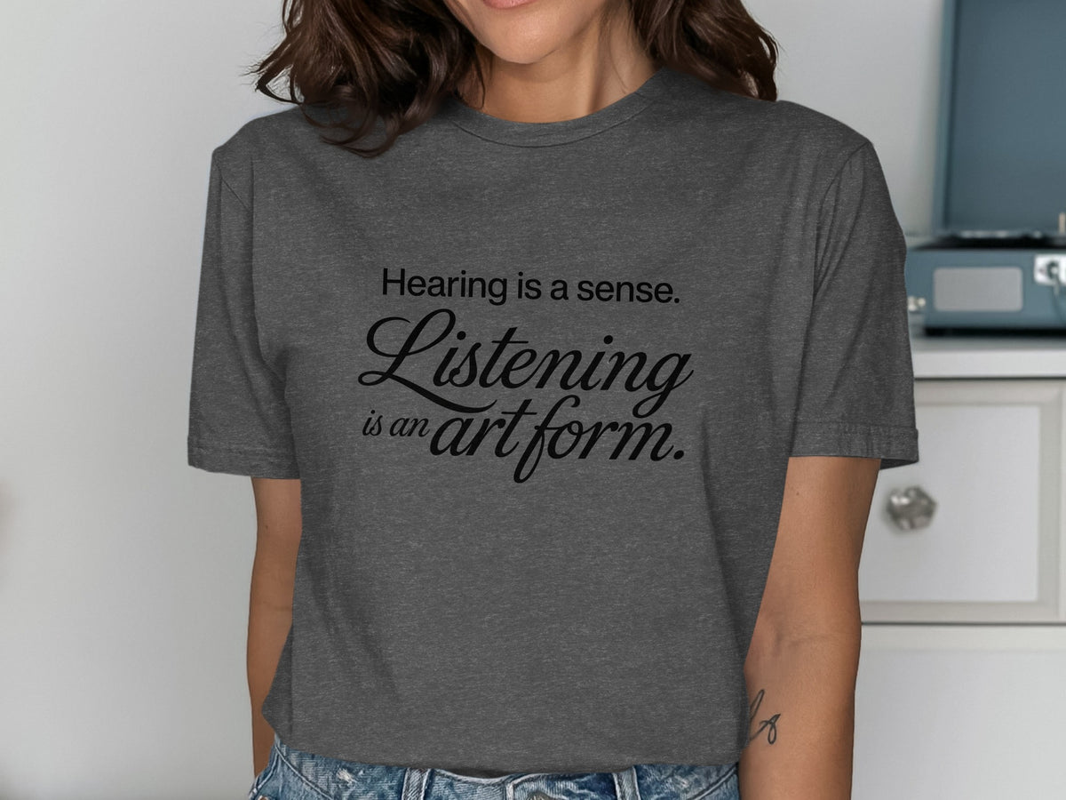 Dark grey t-shirt with black text reading "Hearing is a sense. Listening is an art form."