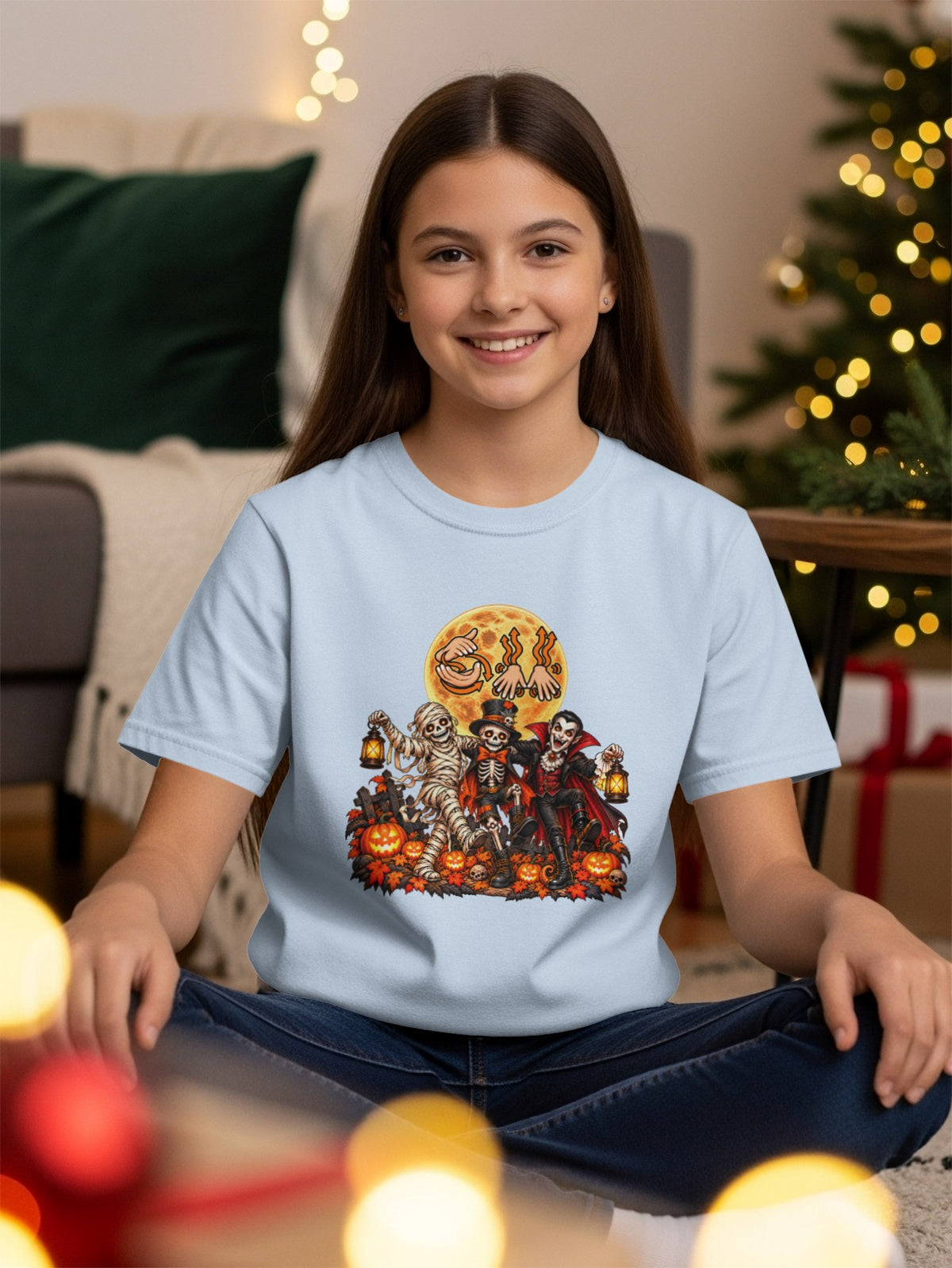 Light blue t-shirt with Halloween characters: mummy, skeleton, and vampire, under a large moon.