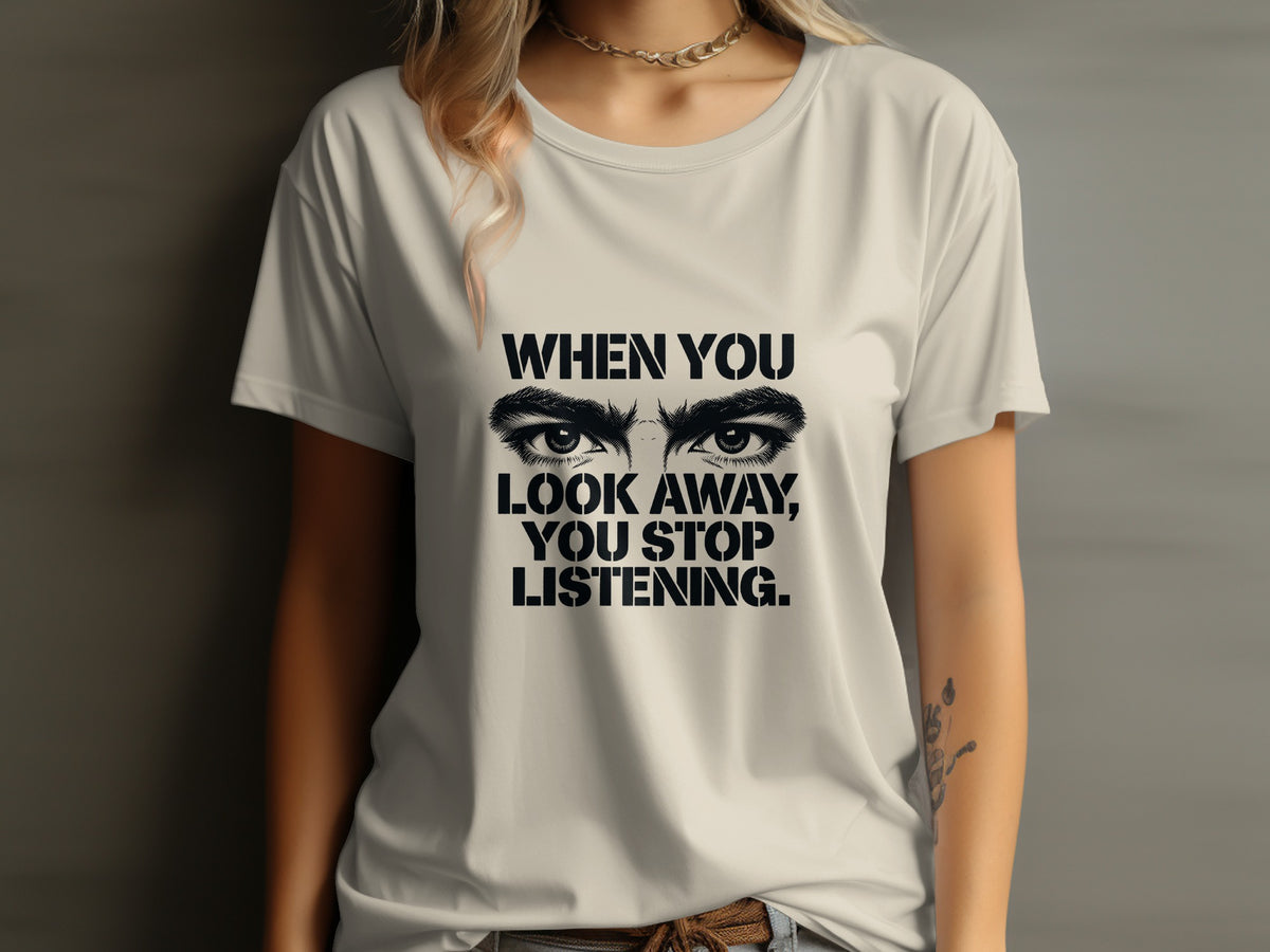 Cream t-shirt with text and eyes graphic reading "WHEN YOU LOOK AWAY, YOU STOP LISTENING."